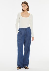 Top bianco a maniche lunghe con scollatura a barco abbinato a pantaloni in denim blu scuro larghi con tasche laterali e vestibilità comoda.