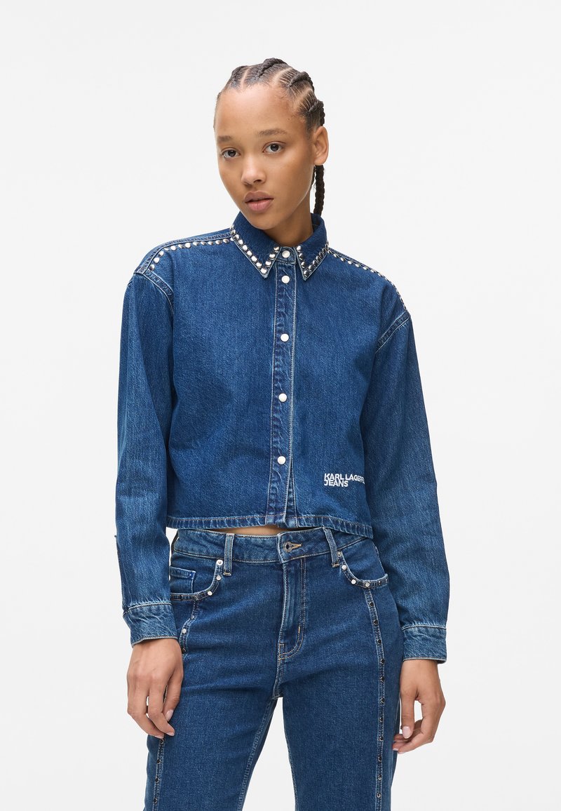 Giacca in denim cropped con chiusura a bottoni, colletto borchiato e ricamo "KARL LAGERFELD JEANS" sull'orlo. Colore blu intenso, tessuto testurizzato.