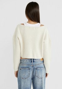 Suéter corto de punto blanco con un ajuste holgado y mangas anchas, combinado con unos pantalones vaqueros de corte alto de denim azul claro.
