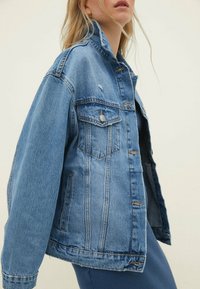 Světle modrá džínová bunda se klasickým střihem, obsahující dvě přední kapsy, zapínání na knoflíky a mírně třepící se detaily na spodním lemu.