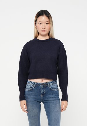 Pull très court bleu marine avec manches longues, motif tricot texturé et col rond, associé à un jean bleu.