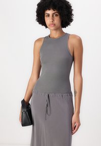 Robe sans manches grise avec un corsage ajusté et une taille à cordon, accompagnée d'un petit sac à main noir. Texture douce et côtelée.