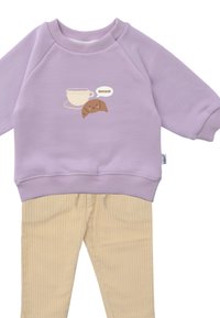 Lavendel-Sweatshirt mit süßem Becher- und Croissant-Graphic; kombiniert mit strukturierten beigefarbenen Cordhosen mit verstellbarem Bund.