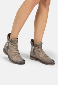 Botines de piel topo con diseño arrugado, perforaciones decorativas, cremallera lateral expuesta y un bajo tacón de madera.