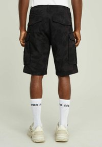 Czarne szorty cargo z subtelnym abstrakcyjnym wzorem, z kieszeniami bocznymi, prostym krojem, w połączeniu z białymi skarpetami i jasnymi trampkami.