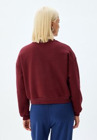 Bordowy sweatshirt o skróconym kroju, z prążkowanymi mankietami i dołem. Gładka tekstura, szerokie rękawy i okrągły dekolt.