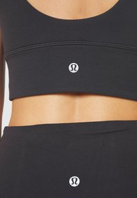 Black sports bra and matching high-waisted leggings with a smooth texture, featuring a small white logo at the center of each garment.