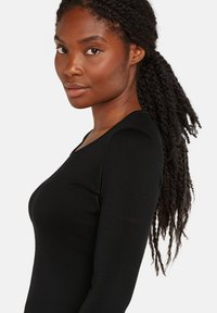 Top negro de manga larga hecho de un material texturizado. Cuenta con un escote en V y un detalle de logo sutil en la manga.