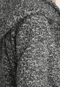 Šedý texturovaný vlněný kabát s volným střihem, který má velký skládací límec a různorodý vzor tkaniny, zdůrazňující teplo a měkkost.