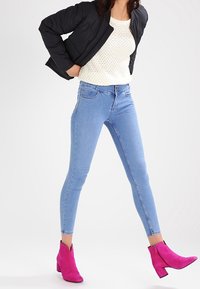 Jeans skinny blu, maglione a maglia beige e giacca pesante nera, abbinati a stivaletti fucsia. Tessuto liscio e design aderente.