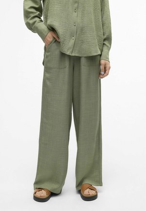 Chemise ample vert clair à boutons et pantalon large assorti avec poches avant, porté avec des sandales compensées couleur beige.