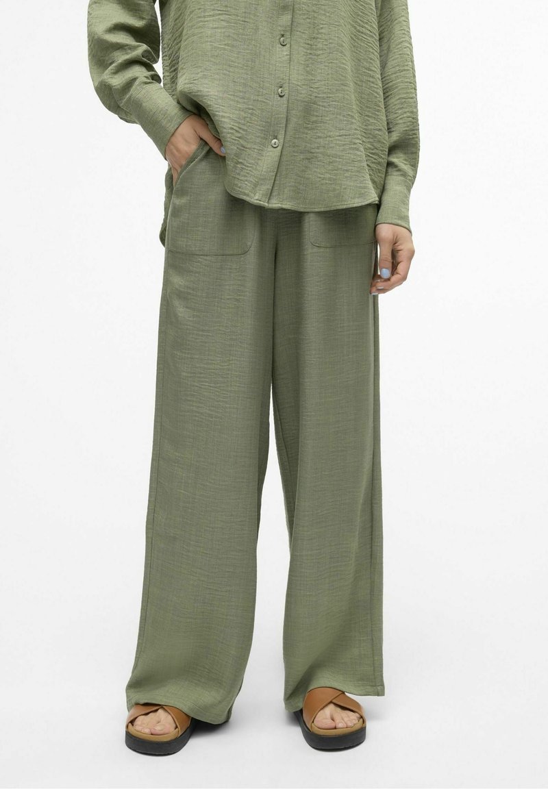 Chemise ample vert clair à boutons et pantalon large assorti avec poches avant, porté avec des sandales compensées couleur beige.