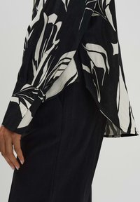 Camicia a maniche lunghe bianca e nera con un audace motivo fogliare, vestibilità casual, tessuto leggero e orlo curvo con polsini abbottonati.