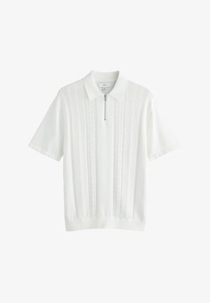 Bela polo majica s kratkimi rokavi in zadrgo na ovratniku, ki ima teksturirane navpične vzorce in rebrast rob na dnu in rokavih.