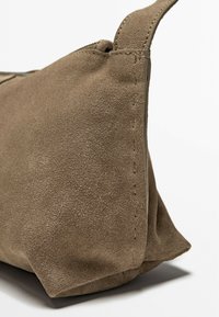 Borsa in suede marrone con superficie texturizzata, caratterizzata da un evidente dettaglio di cucitura lungo il lato e una chiusura con zip sulla parte superiore.