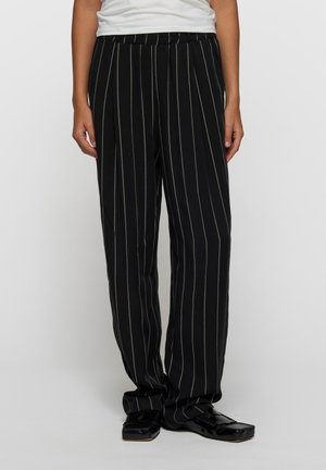 Czarne spodnie w paski z elastycznym paskiem w talii. Posiadają pionowe białe cienkie paski i luźny krój. Materiał wydaje się miękki i lekki.