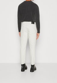 Pantaloni bianchi a sigaretta con una finitura testurizzata e due tasche posteriori. Abbinati a una maglietta nera a maniche lunghe e stivali neri.