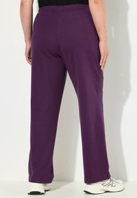 Pantalons violets, fluides, avec taille élastique et coupe droite, en tissu doux, associés à des chaussures de sport blanches.