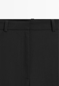Close-up of black trousers waistband with belt loops and concealed front fastening detail.