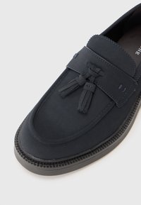 Navyblaue Wildleder Slipper mit Quastendetails, abgerundetem Zehenbereich und kontrastierenden Nähten. Verfügt über eine strukturierten Gummisohle für besseren Halt.
