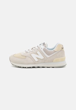 Baskets New Balance beige et blanches avec panneaux en mesh et en suède, design à lacets et semelle épaisse texturée, vues de côté.