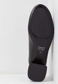 Semelle d'une chaussure en cuir noir à talon carré, étiquetée Filippa K, fabriquée au Portugal, taille 37, présentée sur un fond blanc.