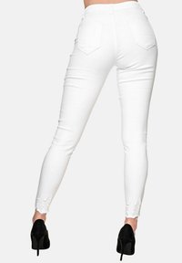 Jeans blancos de cintura alta con un diseño ajustado, que presentan detalles desgastados en los tobillos. Combinados con zapatos de tacón alto negros.