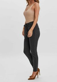 Béžový bezrukávový body kombinovaný s tmavě šedými kalhotami ve stylu jogger s elastickým pasem a bočními kapsami, doplněný hnědými vysokými podpatky.