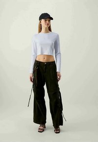Balts garais piedurkņu cropped tops, olīvu krāsas cargo bikses ar sānu siksnām, melna cepure un melnas siksnām sandales. Viegls audums, brīvs griezums.
