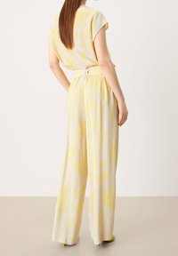 Yellow floral jumpsuit with a relaxed fit, short sleeves, and belted waist; lightweight fabric with a smooth texture.