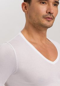 Weißes V-Ausschnitt-T-Shirt aus leichtem Baumwollstoff. Verfügt über ein körpernahes Design mit glatter Textur und kontrastierenden weißen Akzenten am Halsausschnitt.