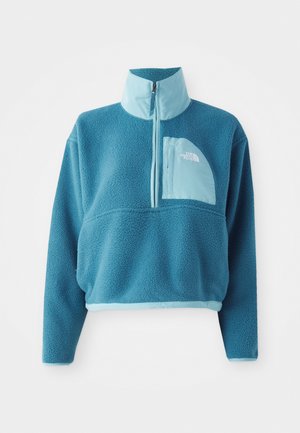 Blå fleece genser med delvis glidelås, høy krage og en foran lomme. Utsmykket med en lysere blåkant og teksturert stoff.