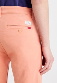 Levi's peach-colored pants with a back pocket, button detail, and a Levi's label. Smooth texture with no visible patterns.