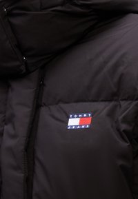Veste matelassée noire avec un petit patch logo Tommy Jeans aux couleurs rouge, blanc et bleu sur la poitrine.
