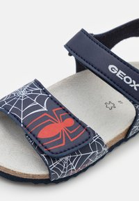 Modré a černé sandály s vzorem pavučiny a červeným akcentem ve tvaru pavouka, nastavitelné pásky a texturovaná gumová podešev.