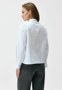 Krótka biała koszula z delikatnym wzorem w kropki, z długimi rękawami i mankietem na guziki, zestawiona z ciemnoszarymi, wysokim stanem jeansami.