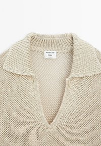 Beige gebreide trui met een V-hals en een gestructureerde kraag. Etiket aan de binnenkant vermeldt "Massimo Dutti Studio Made in Spanje."