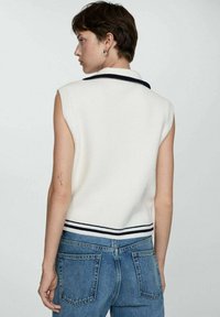 Ærmeløs hvid striktop med krave, marineblå stribede detaljer ved halsudskæringen og i bunden, parret med højtaljede blå denimjeans.