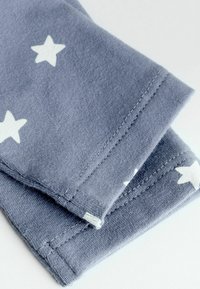 Tissu bleu avec des motifs d'étoiles blanches, montrant un gros plan des bords repliés et des coutures détaillées sur un matériau doux.