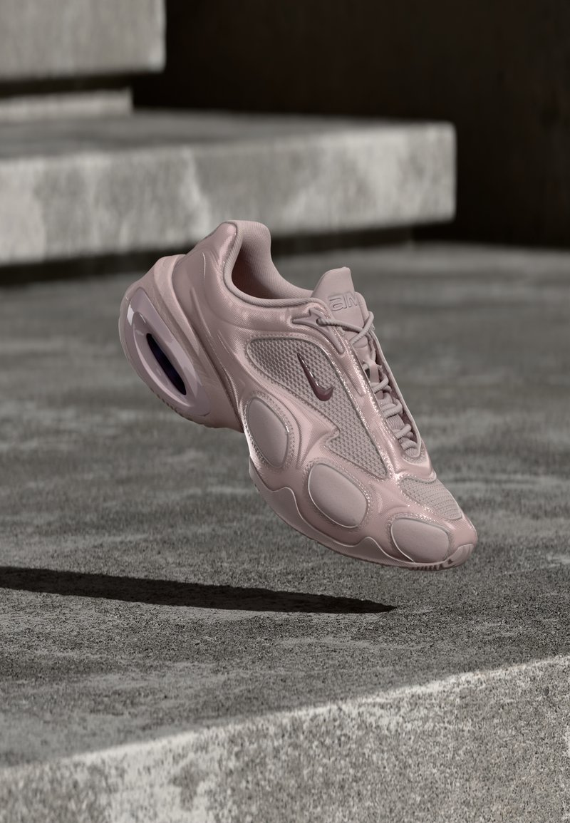 Αθλητικό παπούτσι Nike σε ανοιχτό ροζ, με επάνω μέρος από δίχτυ, στρογγυλεμένη σόλα και ορατή απορρόφηση κραδασμών. Ομαλή υφή με ανάγλυφες λεπτομέρειες.