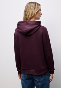 Sudadera burdeos vista desde atrás, con capucha ajustable y dobladillo acanalado. La tela suave y el corte relajado complementan el diseño.