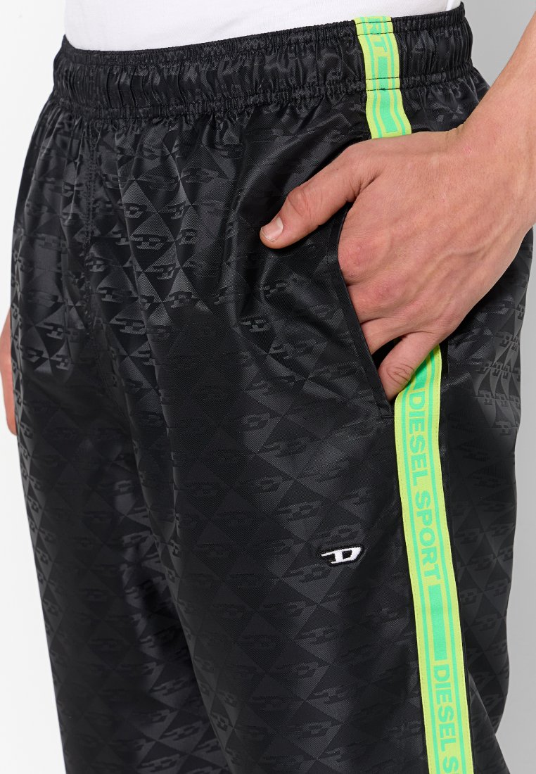 Mano nella tasca dei pantaloni da tuta neri con motivo, striscia laterale neon verde "Diesel Sport" e vita elasticizzata.
