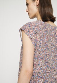 Blusa com padrão floral em tecido leve; apresenta mangas curtas, gola redonda e uma mistura de cores vermelha, azul e creme.