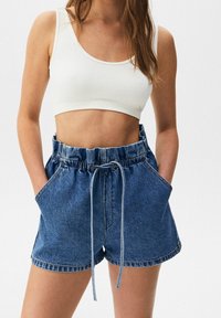 Shorts de mezclilla de cintura alta, con cierre de cordón y bolsillos laterales. Top corto blanco de canalé. Ajuste casual y relajado.