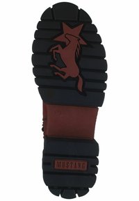 Suela de goma negra con profundas ranuras, con un logo de estrella y caballo en marrón. Material superior rojo con etiqueta en relieve "MUSTANG".