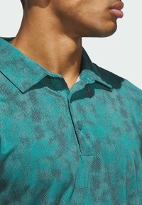 Turquoise button-up shirt with a textured pattern, featuring a collar and subtle gray accents. Close-up view of fabric details.