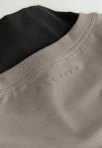 Cămașă de îmbrăcăminte sportivă, cu un material texturat de culoare gri și guler negru, margini cusute și detaliu cu logo-ul „ACTIVE” modelat.
