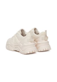 Zapatillas de deporte beige claro con parte superior de tejido texturizado, suela de goma gruesa y un patrón de tracción pronunciado. Cuenta con una lengüeta y un diseño estructurado.