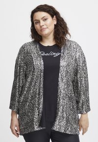 Ezüst flitteres kimono, laza szabással, széles ujjakra és enyhén nyitott elülső részre jellemző. Fekete grafikás póló fölött viselve.