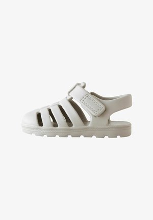 Baltas sandales ar slēgtu purngalu, vairākiem izgriezumiem ventilācijai, Velcro jostu un rakstainu zoli labākai saķerei.